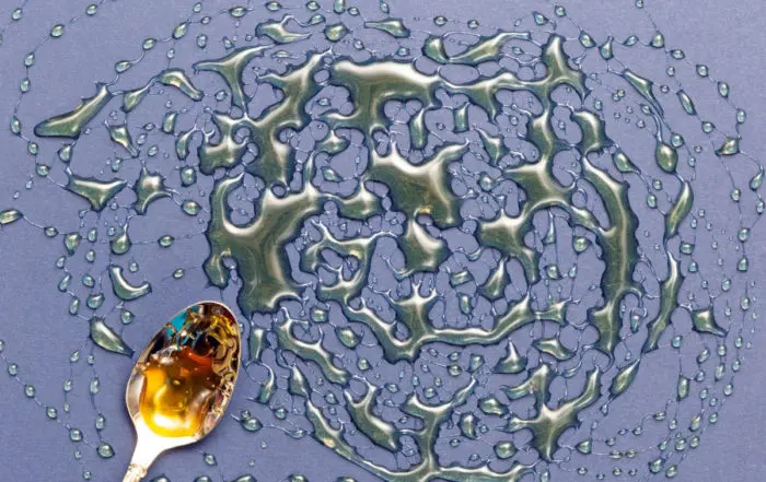 Ein goldener Löffel mit Brausirup für das Bierbrauen, kunstvoll auf einem grauen Hintergrund verteilt.