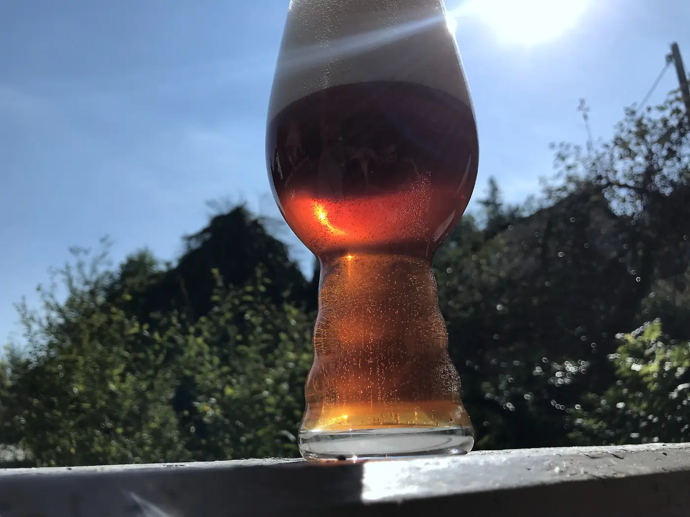 Ein klares, bernsteinfarbenes Bier in einem Glas nach dem Umdrücken vor einem sonnigen Hintergrund im Freien.